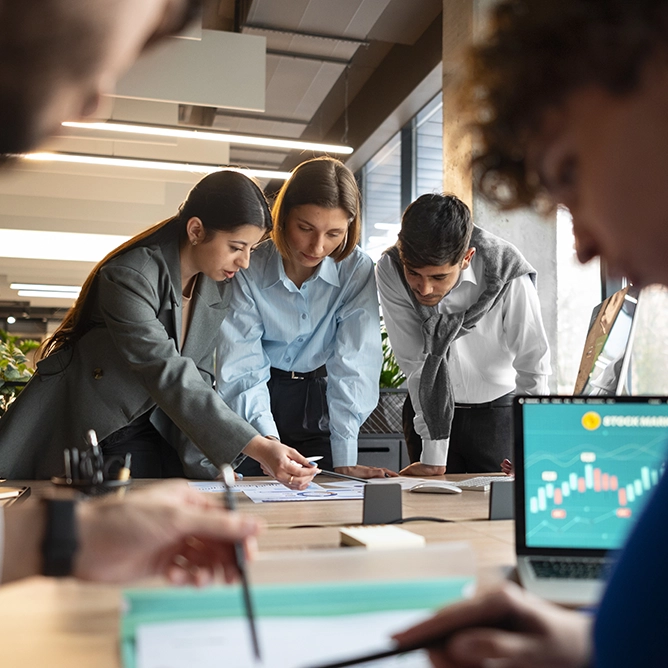 Deux personnes se retrouvent autour d'une table de travail en extérieur, utilisant un smartphone et une tablette tout en discutant. Des carnets et un stylo sont visibles en arrière-plan, mettant en valeur un environnement collaboratif.